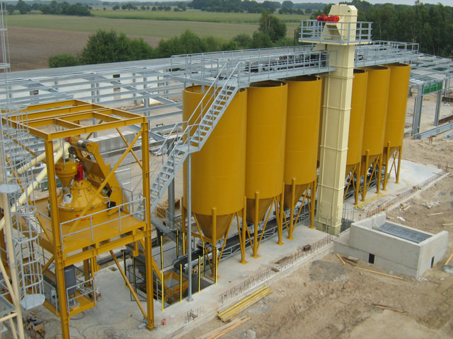 Becherwerk abgebildet mit 6 gelben Silos und einem Betonmischer.