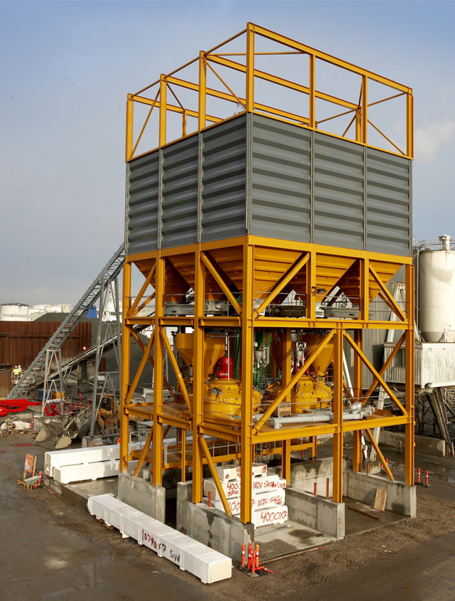 Materialsilos und Mischer in einem robusten, gelben Gestell montiert.